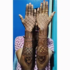 A full coverage bridal mehendi design shown by a happy client. This piece combines a classic checkerboard pattern on the palms with peacock and lotus motifs on the forearms.