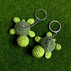 A top-down view of two of my green turtle keychains against a grassy background. The two-tone green gives them a lovely, detailed look.