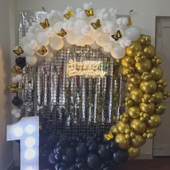 An elegant and chic first birthday setup. The circular balloon arch in black, gold, and white is accented with butterfly details and a shimmering silver backdrop. The light-up number '1' adds a touch of glamour to the celebration.
