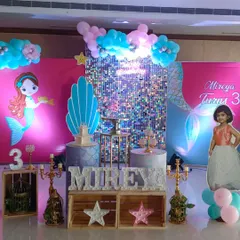 For this third birthday, I created a full mermaid theme. The setup includes a silver shimmer wall for sparkle, character cutouts, a personalized life-size cutout of the birthday girl, and themed pedestals for the cake and desserts.