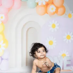 A moment of messy delight during a first birthday cake smash. The daisy-themed backdrop adds a sweet touch.