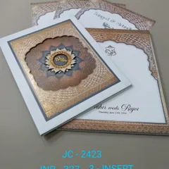 A premium boxed invitation with an intricate, multi-layered mandala design and a custom monogram. The white and bronze color scheme is elegant, and the set includes three inserts for your events.