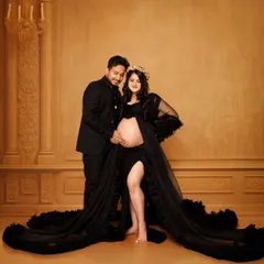 An elegant couple's maternity portrait using a classic painted backdrop. The couple is dressed in formal black, creating a sophisticated and timeless look that focuses on their connection and anticipation.