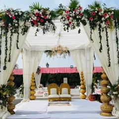 A classic white wedding mandap (Bedi) decorated with hanging floral strings and traditional golden props, perfect for an elegant outdoor ceremony.