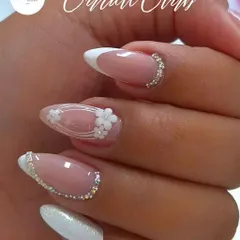 This is a perfect example of a modern bridal look. It features a classic French manicure on an almond nail shape, elevated with delicate 3D white flowers and a precise line of silver rhinestones at the cuticle for a touch of sparkle.