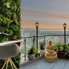 This balcony is a green paradise with a vertical garden wall. A high-top table and chair provide a perfect spot for morning coffee, while a Buddha statue adds a sense of tranquility against the city skyline.