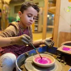 Concentration and creativity come together in this moment. He is carefully painting his freshly made pottery, adding a personal touch of color and design.