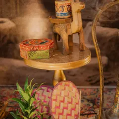 The small details that create an authentic atmosphere. A wooden camel figurine, a hand-painted box, and traditional woven fans bring the essence of Punjabi culture to this decor setup.