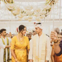 A classic South Indian wedding moment, as the couple makes their way through the crowd under a canopy of jasmine flowers. The bride's golden Kanjeevaram saree and the groom's traditional attire shine in this beautiful, candid shot.