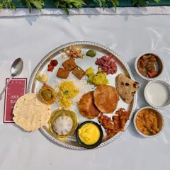 A complete Maharashtrian thali served during a Pangat. The plate is filled with a variety of authentic dishes, including puris, vegetables, dal, rice, and of course, a sweet modak, offering a true taste of Maharashtra.