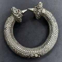 An exclusive silver leg kada, or anklet, with an antique finish. This piece features intricate scaling detail and two ornate heads with ruby-red stone eyes, a truly unique piece of tribal-inspired jewellery.