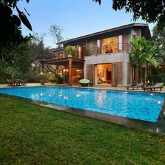 The Mango House in Alibag, seen from the garden. The design features a large swimming pool and an open ground floor that connects directly to the outdoors, blurring the lines between the built structure and the natural landscape.