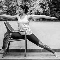 Here, a chair provides support in a modified Virabhadrasana II, or Warrior Pose. This allows you to experience the full benefits of the pose, like opening the hips and strengthening the legs, without straining.