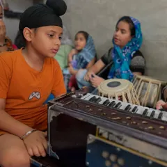 A young student learns harmonium and tabla in a group setting, fostering a collaborative learning environment.
