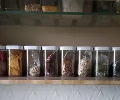 This is the 'after' shot of a well-organized pantry shelf. Using clear, airtight containers for dals, grains, and snacks not only keeps food fresh but also allows you to see exactly what you have at a glance. This simple step prevents overbuying and reduces food waste.
