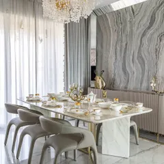 A formal dining room where every detail is considered. The space features a stunning marble table, grey leather chairs, and a dramatic accent wall with book-matched grey marble, all under a beautiful floral-inspired chandelier.
