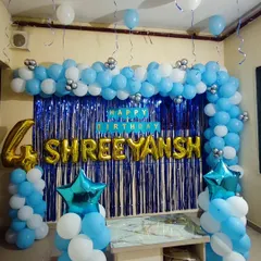 A classic blue and white balloon arch decoration for a fourth birthday. This setup includes a blue shimmer backdrop, the name "SHREEYANSH" in large gold foil letters, and star-shaped foil balloons for extra detail.