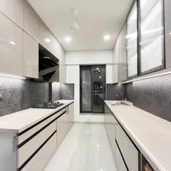 A modern parallel kitchen in a light grey finish. The design includes a long wall unit with a fluted glass shutter, a light quartz countertop, and a bold black textured backsplash for a chic, contemporary feel.