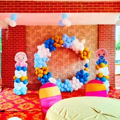 A bright and cheerful setup for a Kuan Pujan ceremony. The decoration includes a circular balloon ring in blue, white, and yellow, with cute baby-themed pillars on each side.