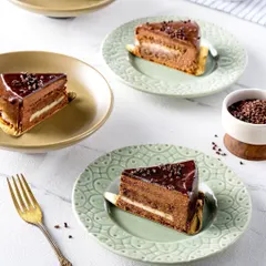 Slices of a rich, multi-layered chocolate pastry served on elegant plates. The bright, clean lighting highlights the glossy ganache and different textures within the cake, creating a look of pure indulgence.