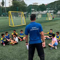 A sports psychologist addresses a group of young, attentive players sitting on the pitch. This image highlights our focus on mental conditioning, a key component of our elite Xcelerate Program.