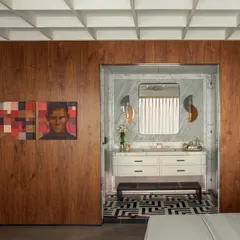 A view from the bedroom into the powder area, showcasing a blend of modern minimalism and timeless sophistication. The rich walnut paneling of the bedroom contrasts beautifully with the cool marble and geometric flooring of the bathroom.