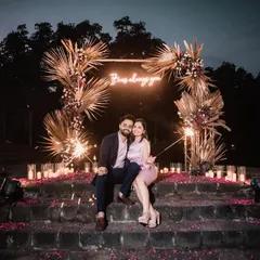 A wide view of our boho-chic proposal setup at dusk. The glowing neon sign, candlelit path, and lush florals against the natural landscape create an incredibly romantic atmosphere.