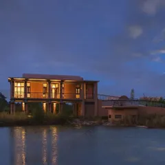 The main building of Waghoba Ecolodge, elevated on stilts, appears to float over the man-made lake at dusk. This design provides stunning, unobstructed views of the forest and minimizes the building's impact on the ground.