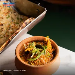 A close-up of a traditional chicken curry served in an earthen pot at Dhaba, alongside fresh naan. This image highlights the authentic presentation and rustic charm of my desi dining experiences.