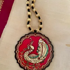 A majestic peacock, brought to life with real Tanjore gold foil against a rich red background. This wearable art piece is sealed with resin to protect its intricate gesso work and brilliant shine, making it a truly royal accessory.