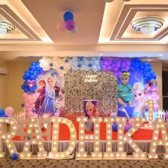 A magical Frozen-themed birthday party for Radhika. The stage includes a silver shimmer wall, character cutouts of Elsa and Anna, and large marquee letters spelling out the name.