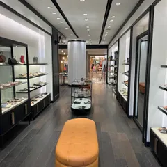 The main walkway of the Pazzion store, showing the clean layout, recessed wall displays with integrated lighting, and a central ottoman for customer seating.