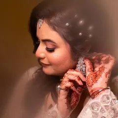 A soft, dreamy shot of a bride getting ready. The focus on her hands, adorned with mehndi, as she puts on her earrings, tells a story of tradition and anticipation.