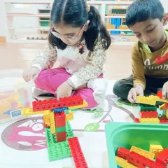 Two children working side by side on their simple machines. Even at a young age, they learn to share the space and materials, building early social skills.
