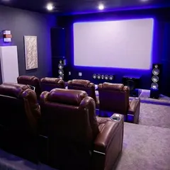 A classic home theater layout with two rows of dark leather recliners on tiered platforms. This setup is enhanced with blue ambient backlighting around the screen, which reduces eye strain and increases perceived contrast for a more comfortable viewing session.