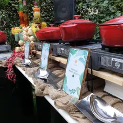 A rustic, picturesque live cooking station set up in a garden. We used burlap runners, wooden crates, and bright red cast-iron pots to create a charming and inviting atmosphere for this outdoor event.