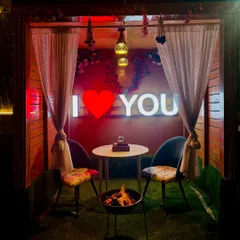 A cozy and private cabana setup perfect for a date night. The "I Love You" neon sign, sheer curtains, and a personal bonfire create an intimate and warm atmosphere for two.