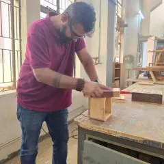 A student carefully sands the edges of a wooden box. The finishing process is just as important as the construction for achieving a professional result.