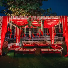 An intimate and traditional seating area for a pre-wedding ceremony. The design uses block-printed fabrics in red and white, with comfortable gaddas and hanging floral tassels.