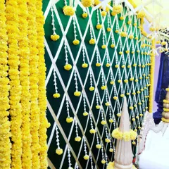 A detailed look at the backdrop of the traditional mantap. It features a lattice pattern of white ribbons over a dark green background, with hanging marigold buds that complement the garlands above.