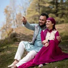 A candid moment in the Himachali countryside, with the couple sharing a laugh while dressed in vibrant traditional outfits.