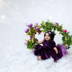 A dreamy portrait of a baby girl on a floral swing, surrounded by soft clouds. This magical setup is perfect for celebrating any milestone, like a half-birthday.