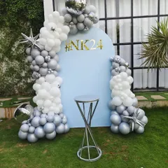 A modern and chic outdoor birthday decoration. This features a custom blue arch backdrop with a personalized hashtag, framed by an elegant silver and white chrome balloon garland.