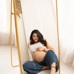 A beautiful moment of self-reflection. The mother-to-be sits before a mirror in casual jeans, creating a thoughtful and artistic portrait that celebrates her changing body.