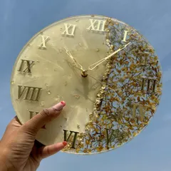 A finished varmala preservation clock, held up to the sky to show the beautiful details of the preserved flowers and gold foil.
