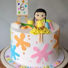 An art-themed cake for a budding artist's 6th birthday. This design features a custom figurine, colorful paint splatters, and an easel.