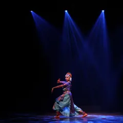 A striking solo performance under three spotlights. The dancer's powerful stance and the dramatic lighting create a captivating visual on the dark stage.