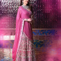 A full-length portrait of Mrs. Nita Ambani, showcasing her magnificent pink and silver lehenga against a shimmering, textured background. The image captures the grandeur and elegance of the sangeet celebration.