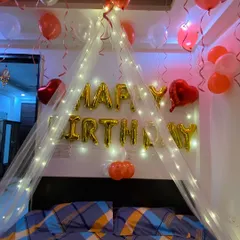 This birthday setup features a beautiful cabana made of sheer fabric and fairy lights over the bed. It creates a cozy and magical focal point in the room, complemented by 'Happy Birthday' foil balloons.