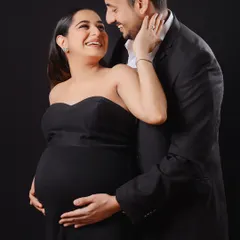 An intimate moment between an expecting couple, both dressed in classic black. This studio portrait focuses on their happy expressions and the shared excitement of their journey.